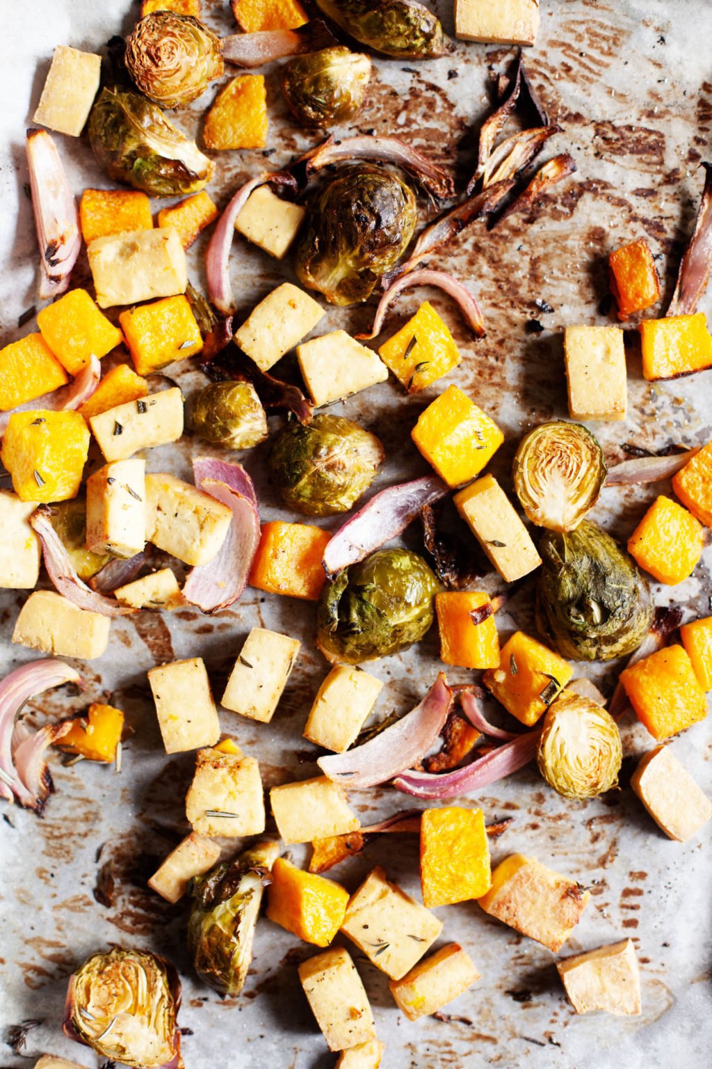A baking sheet is covered with freshly roasted autumn produce and herbs.