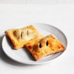 Two rectangular, vegan cherry hand pies with crispy golden pastry sit next to each other on a dessert serving plate.