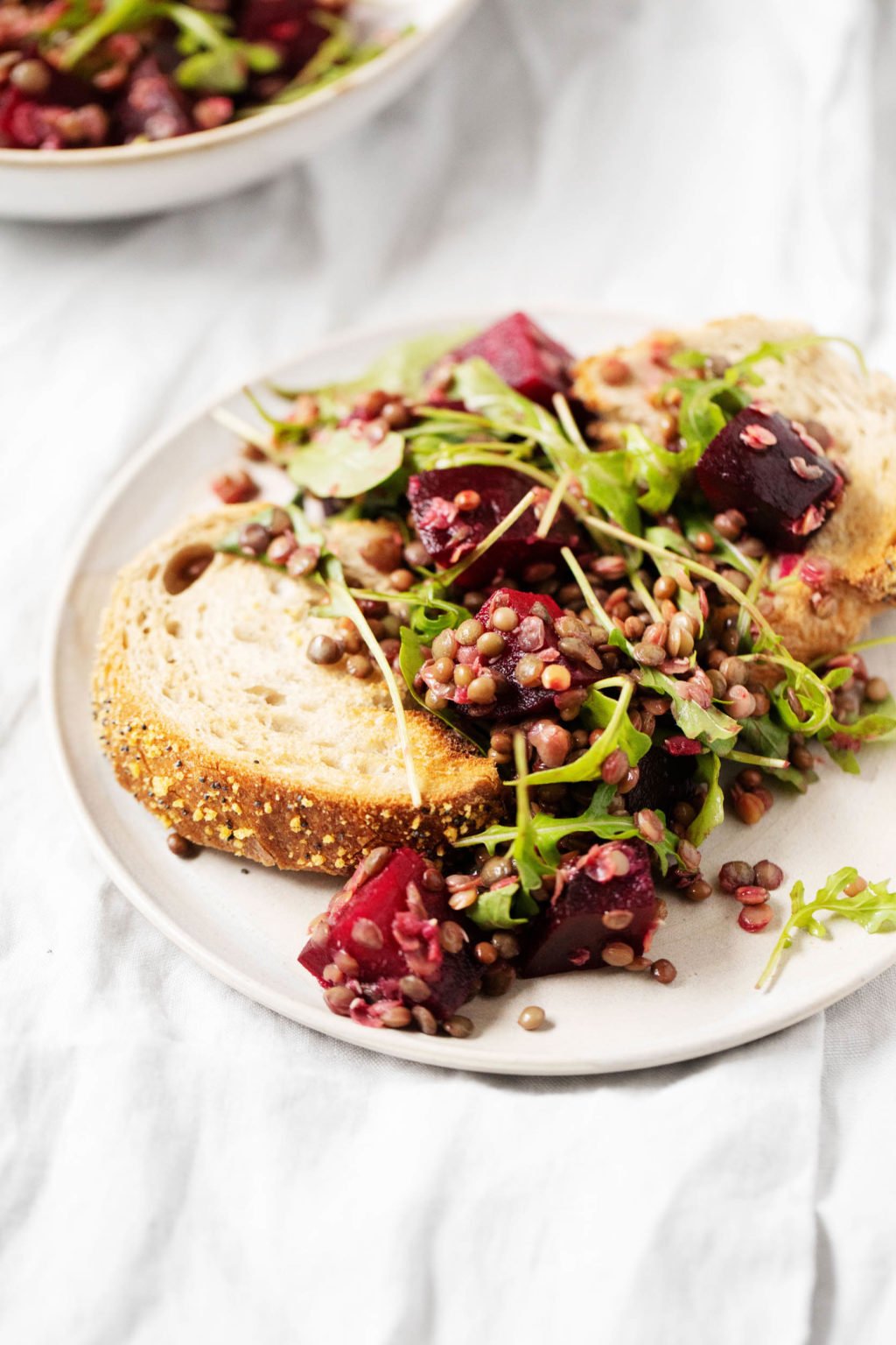 Leftovers of a salad with arugula, beets and lentils are piled over a slice of toast. 