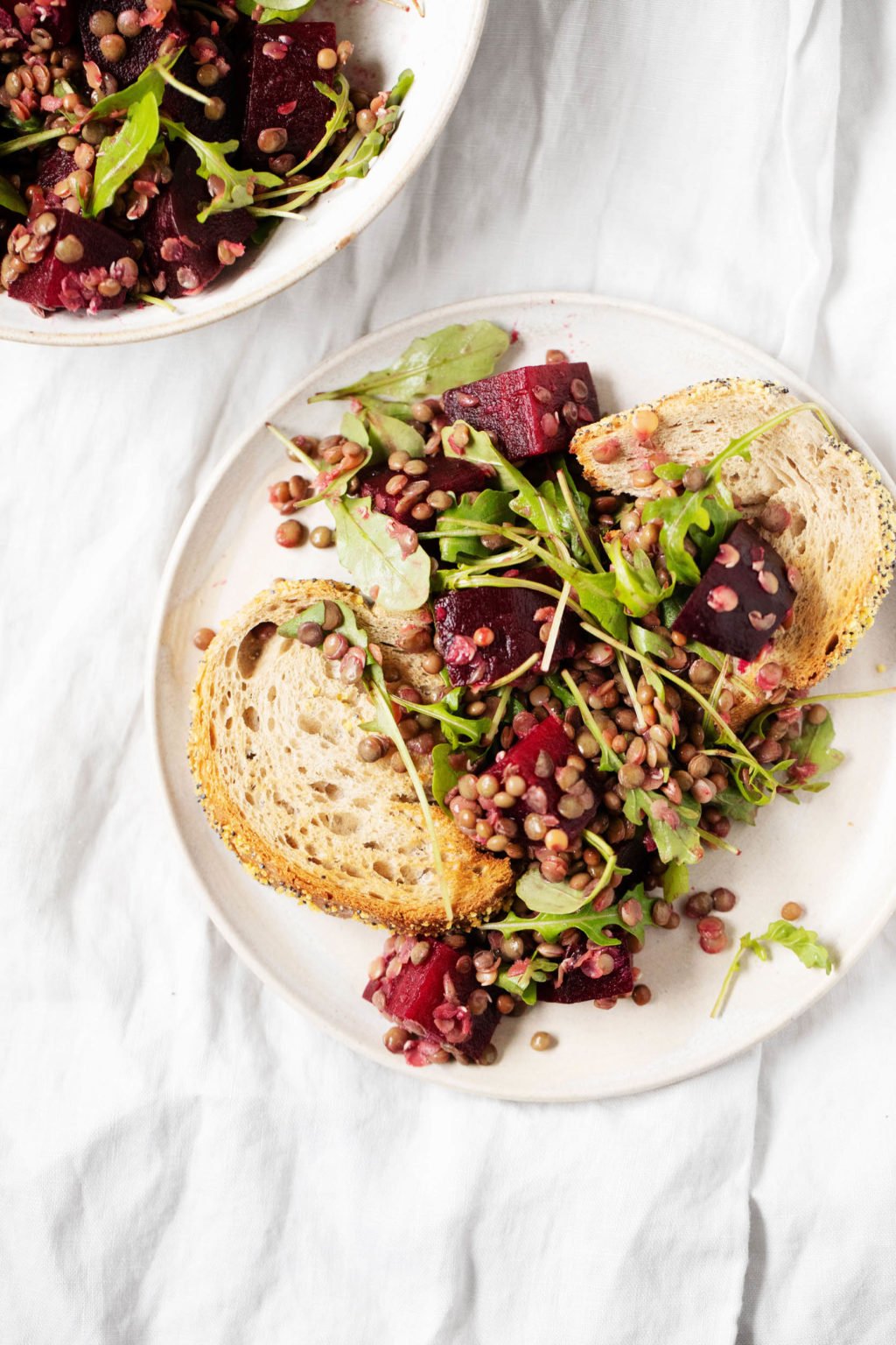 An overhead image of a slice of bread that's been piled with lentils, beets, and arugula.