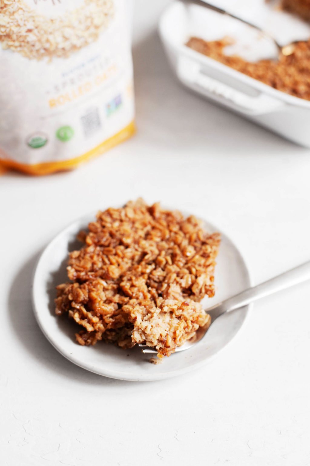 A plate of vegan brown sugar baked oatmeal, with a bag of rolled oats in the background.