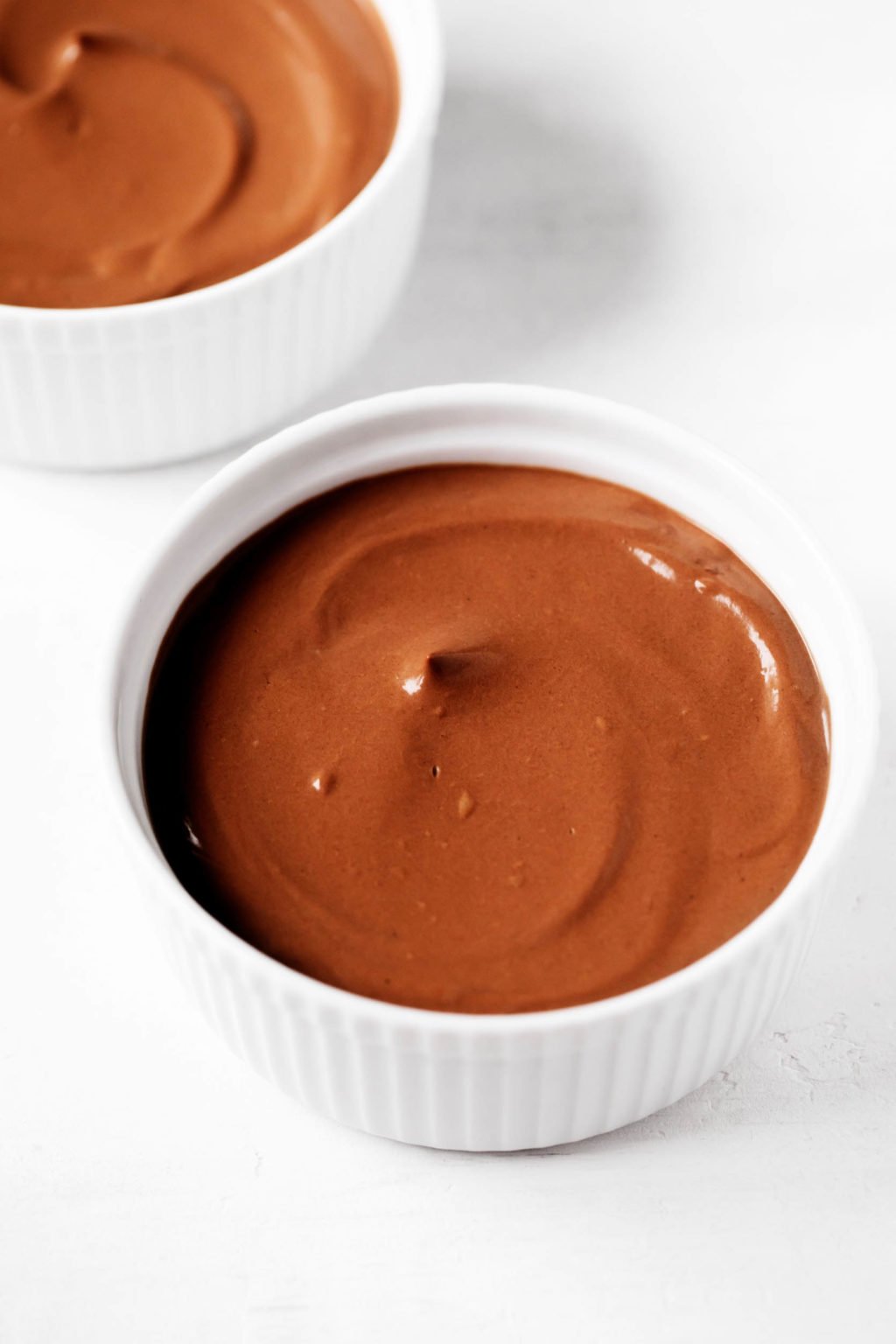 Two white ramekins are filled with a swirled, dairy-free chocolate pudding.