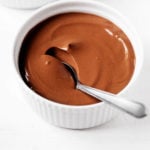 Two ramekins are filled with a creamy vegan silken tofu chocolate pudding. One has just been scooped into with a spoon.