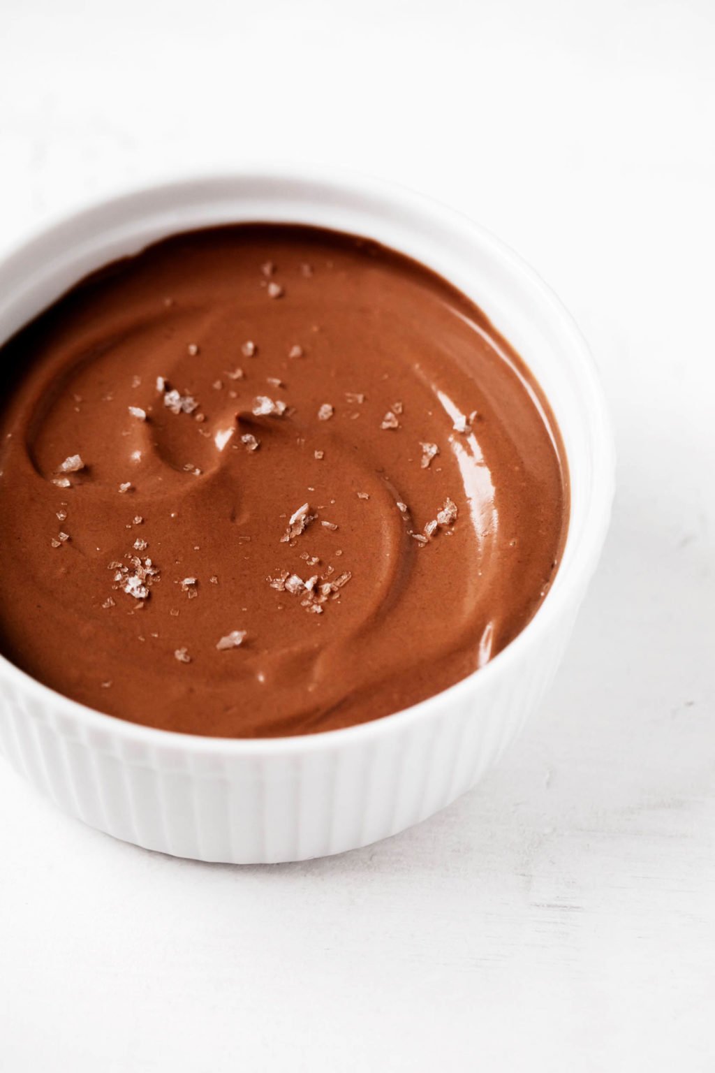 A small, round container of vegan silken tofu chocolate pudding has been topped with flaky sea salt.
