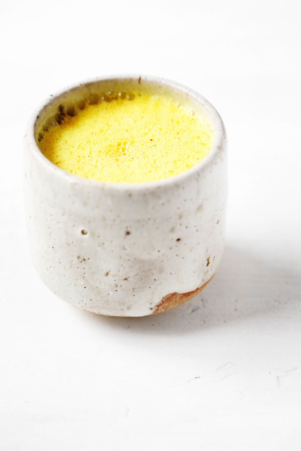A cozy, small mug containing a brightly colored spice blend, mixed with non-dairy milk.