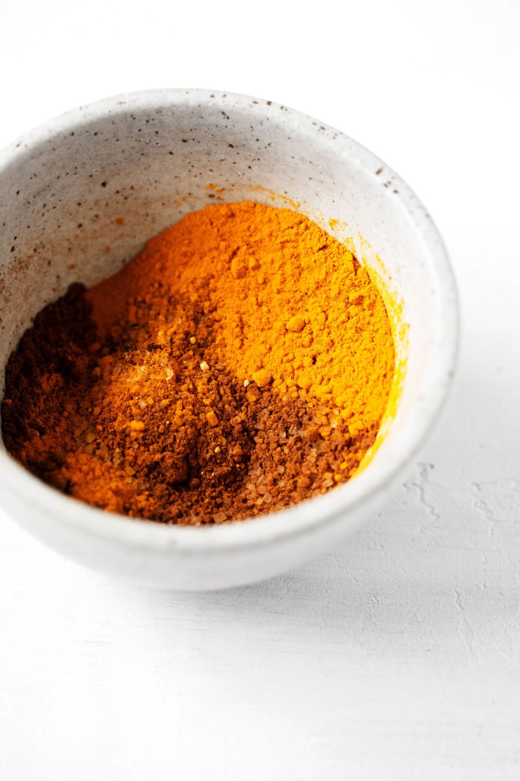 A number of golden-hued spices are mixed together in a small pinch bowl.