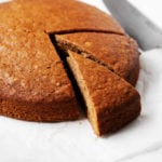 A round, golden brown gingerbread cake is being cut into slices.