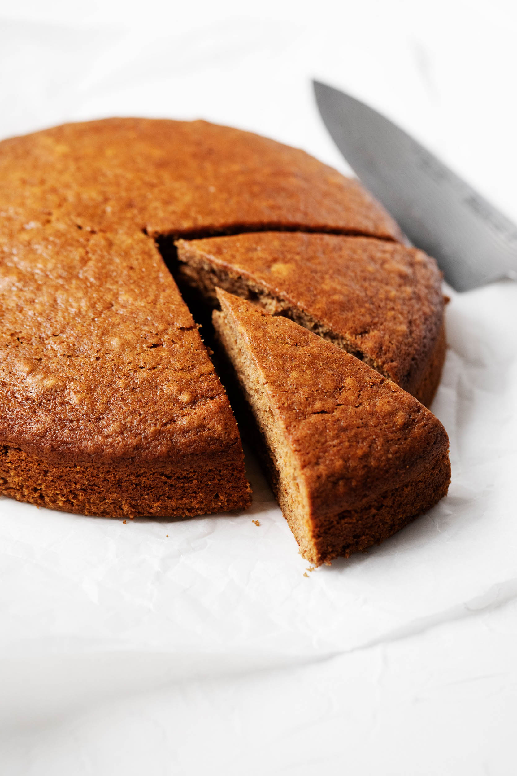 A round, golden brown gingerbread cake is being cut into slices.
