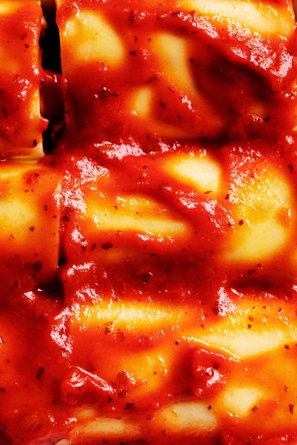 A zoomed in photograph of the top of a baked pasta dish with marinara sauce.