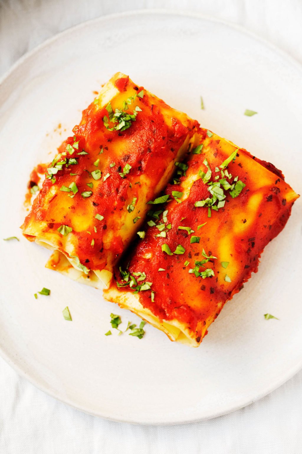 An overhead photo of two vegan lasagna rolls, sprinkled with fresh herbs.