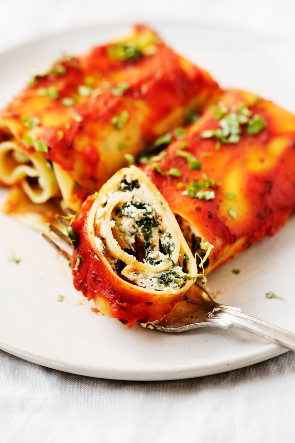 Two plant-based lasagna rolls are on a serving plate, and one of the rolls has just been sliced into.