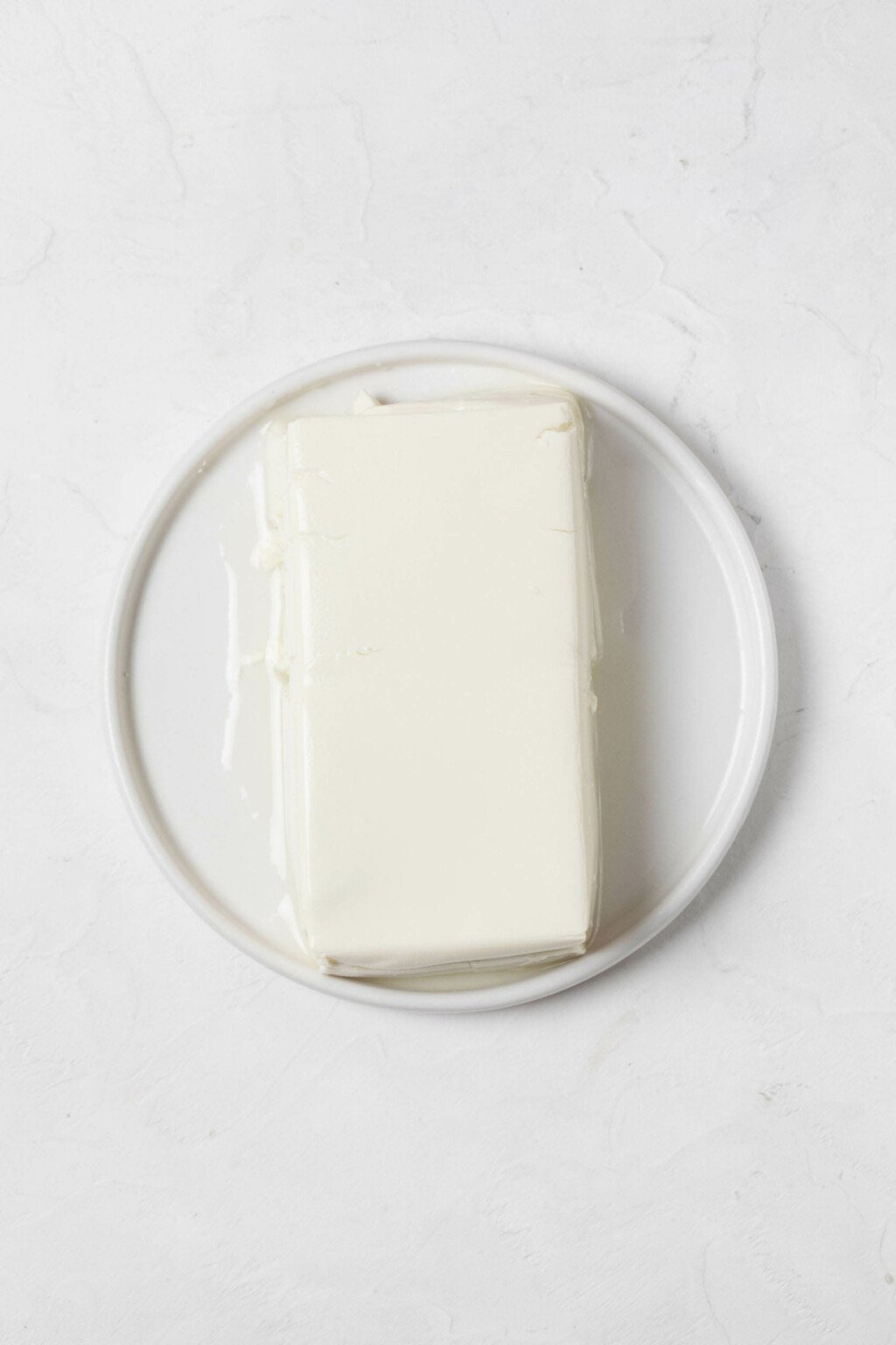 An overhead image of a white block of silken tofu, which is resting on a white plate.