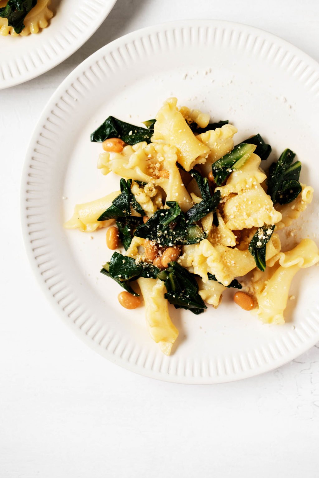 Two white porcelain plates hold portions of a simple, plant-based pasta with beans and greens.