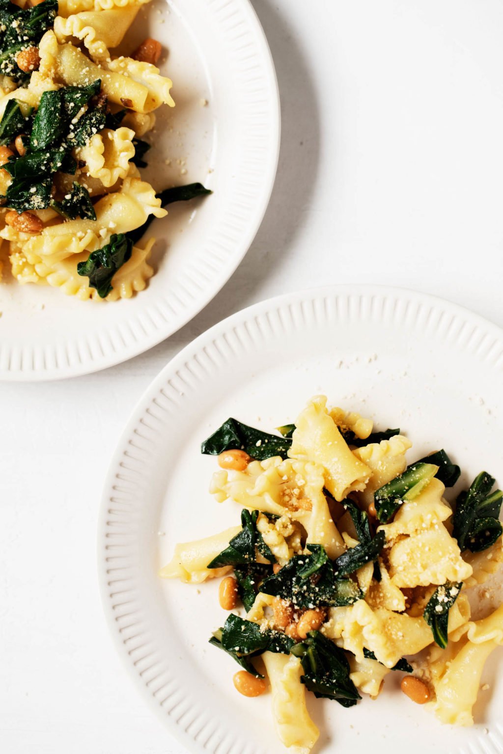 Two white plates are piled with a pasta that's flecked with leafy greens.