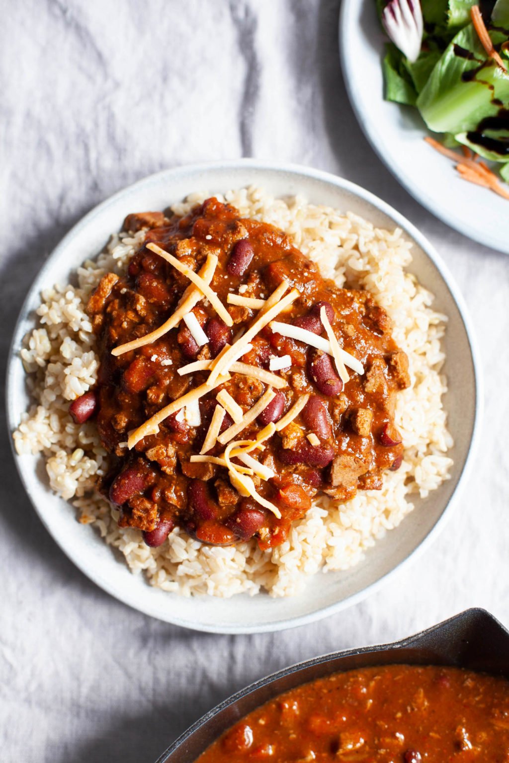 A plant-based tofu chili is topped with vegan cheese and piled over a plate of brown rice.