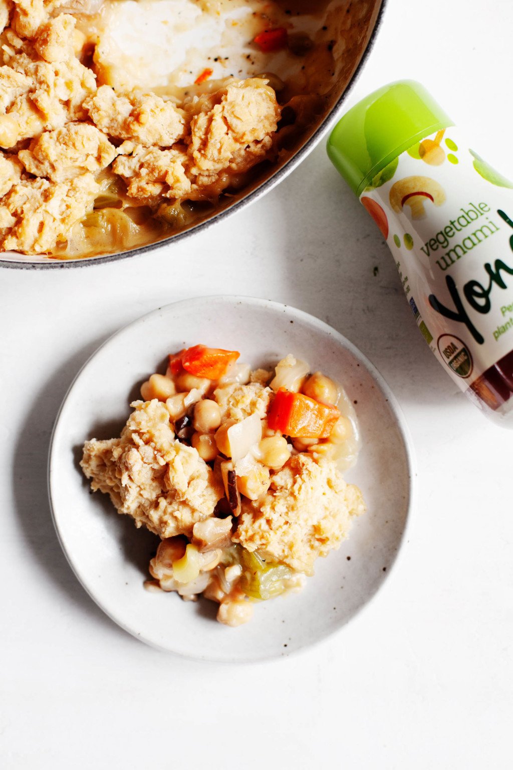 A small serving plate with a savory, wintery vegan chickpea dish, along with a container of savory cooking liquid.