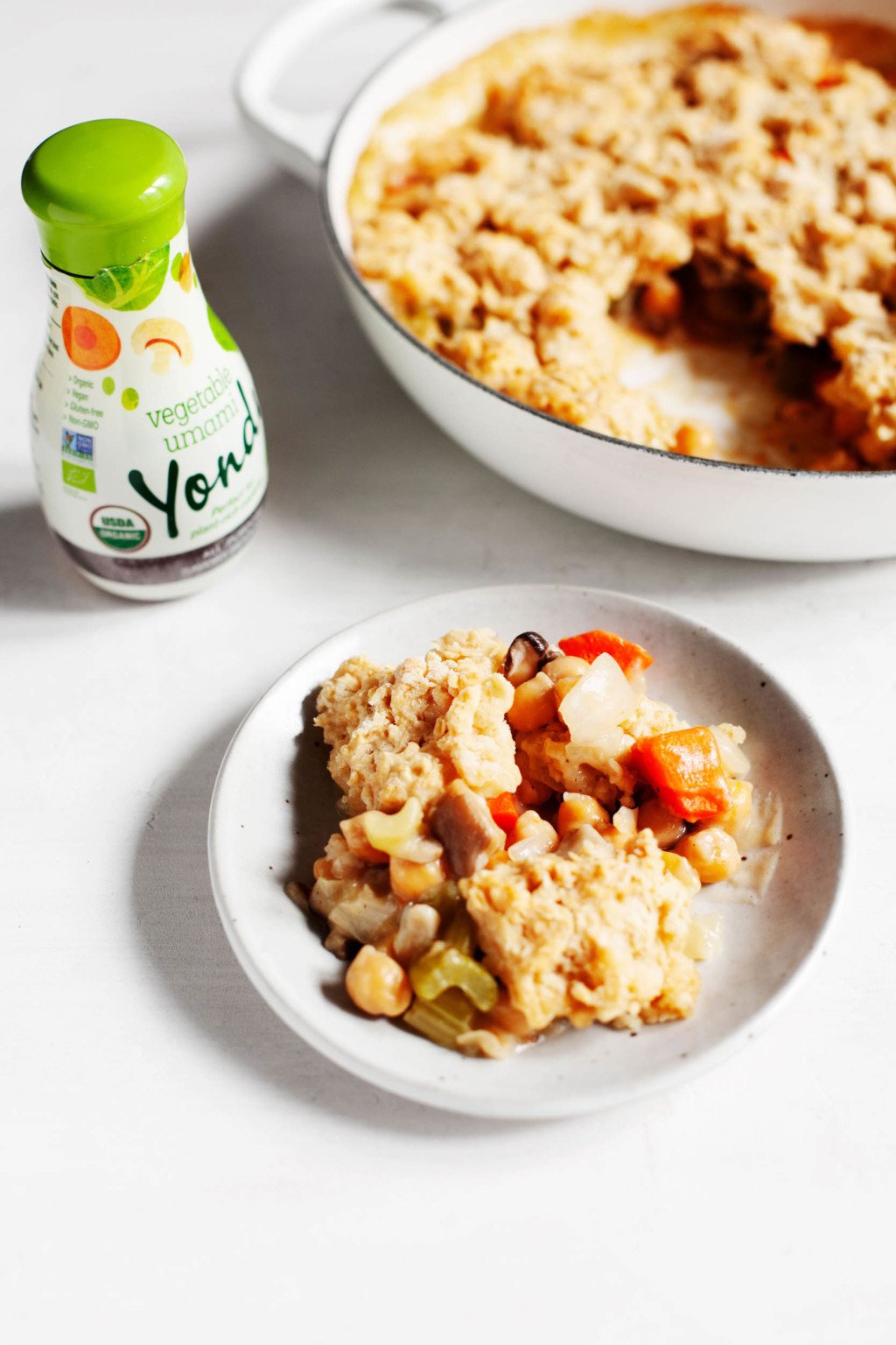 A vegan savory chickpea cobbler has is served on a small plate with the round cooking skillet nearby.