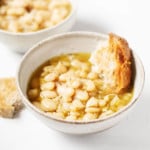 Two matching, white bowls are filled with beans, broth, and torn pieces of fresh bread.