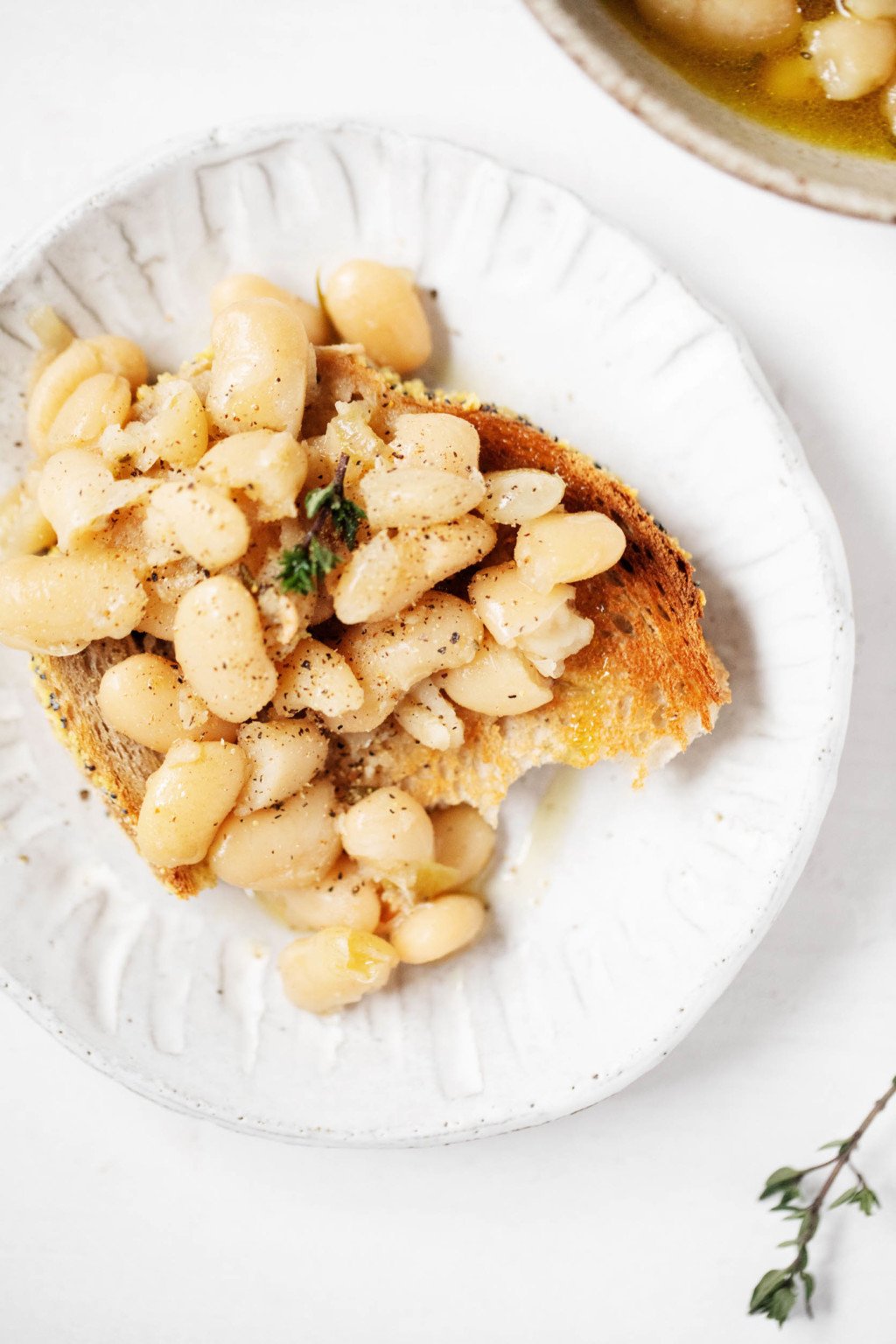 A slice of toast, topped with beans, has been garnished with herbs. It rests on a small, fluted ceramic plate.