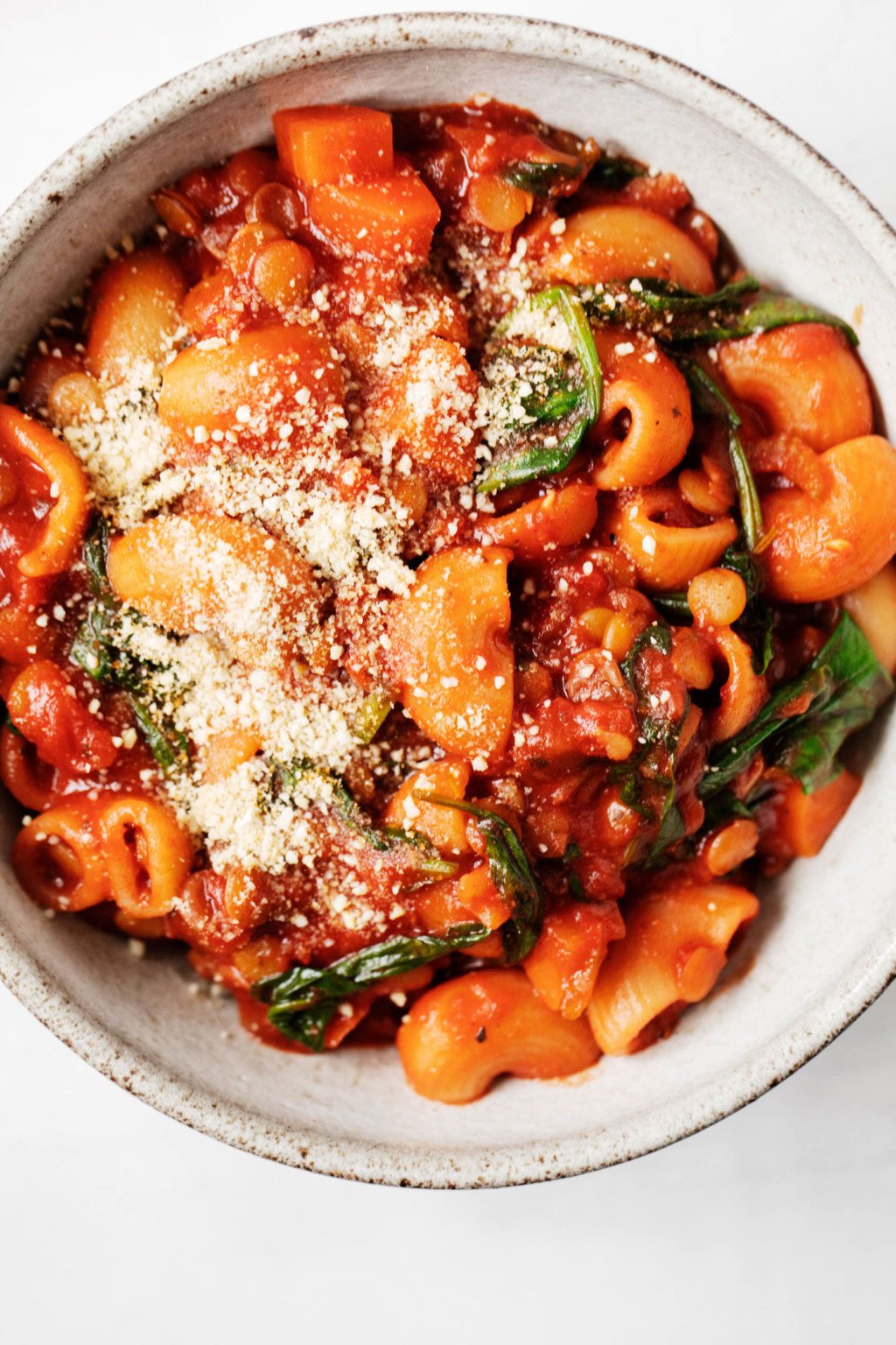 A close up, overhead image of a bowl of vegan lentil tomato pasta stew, made with lumache and wilted greens.
