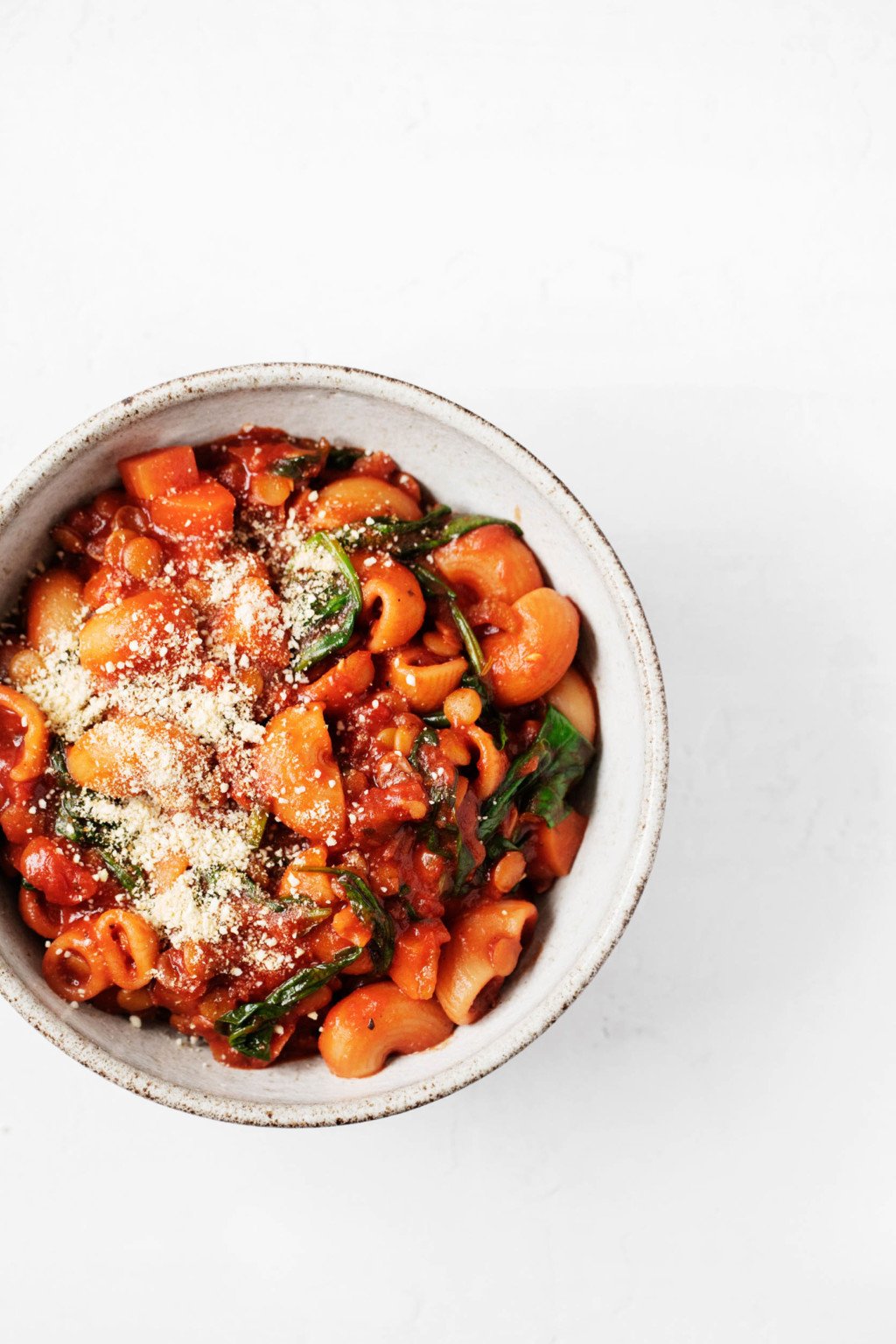 A small bowl of a pasta, lentil, and green dish, which has been topped with ground cashews.