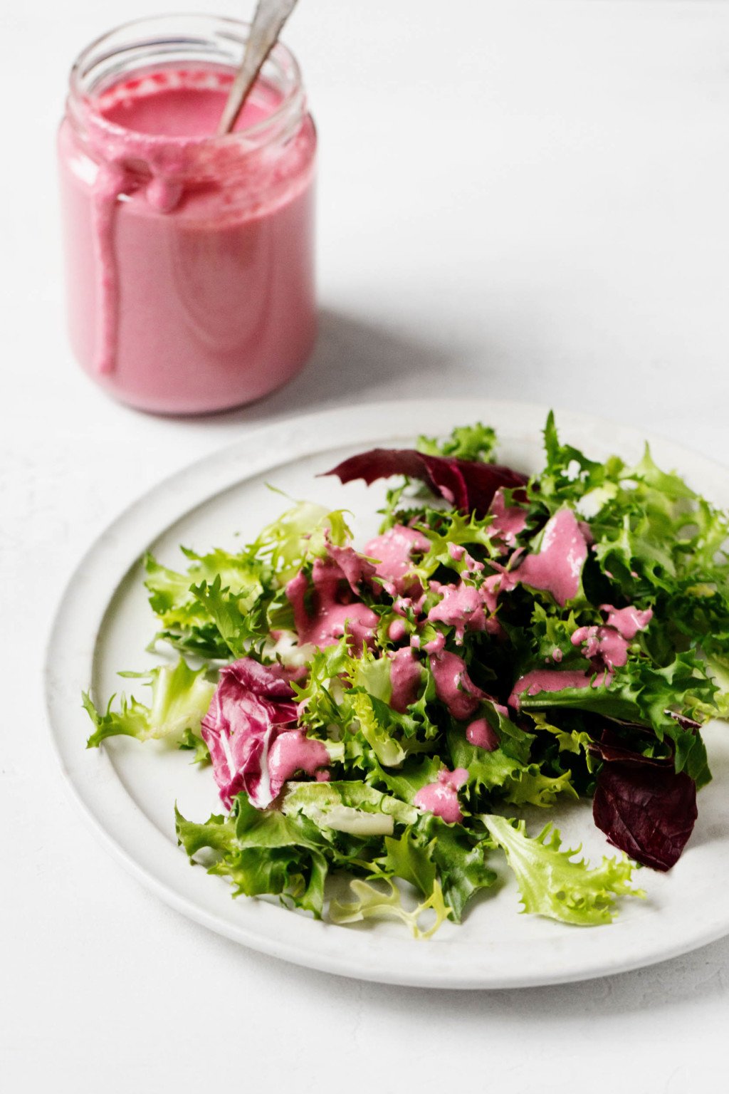 Se ha rociado una pequeña ensalada verde con un aderezo cremoso a base de plantas de color rosa.