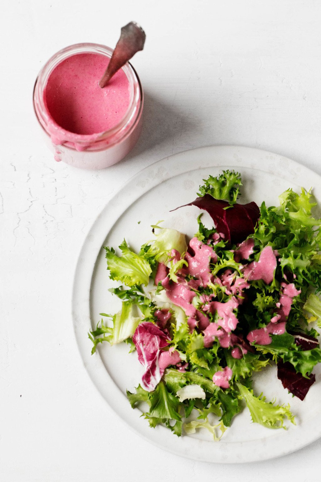 A bed of greens has been dressed with a plant-based, bright pink salad dressing.