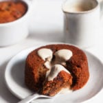 Vegan sticky toffee pudding is on a small dessert plate, with cashew cream sauce and another ramekin of pudding in the background.