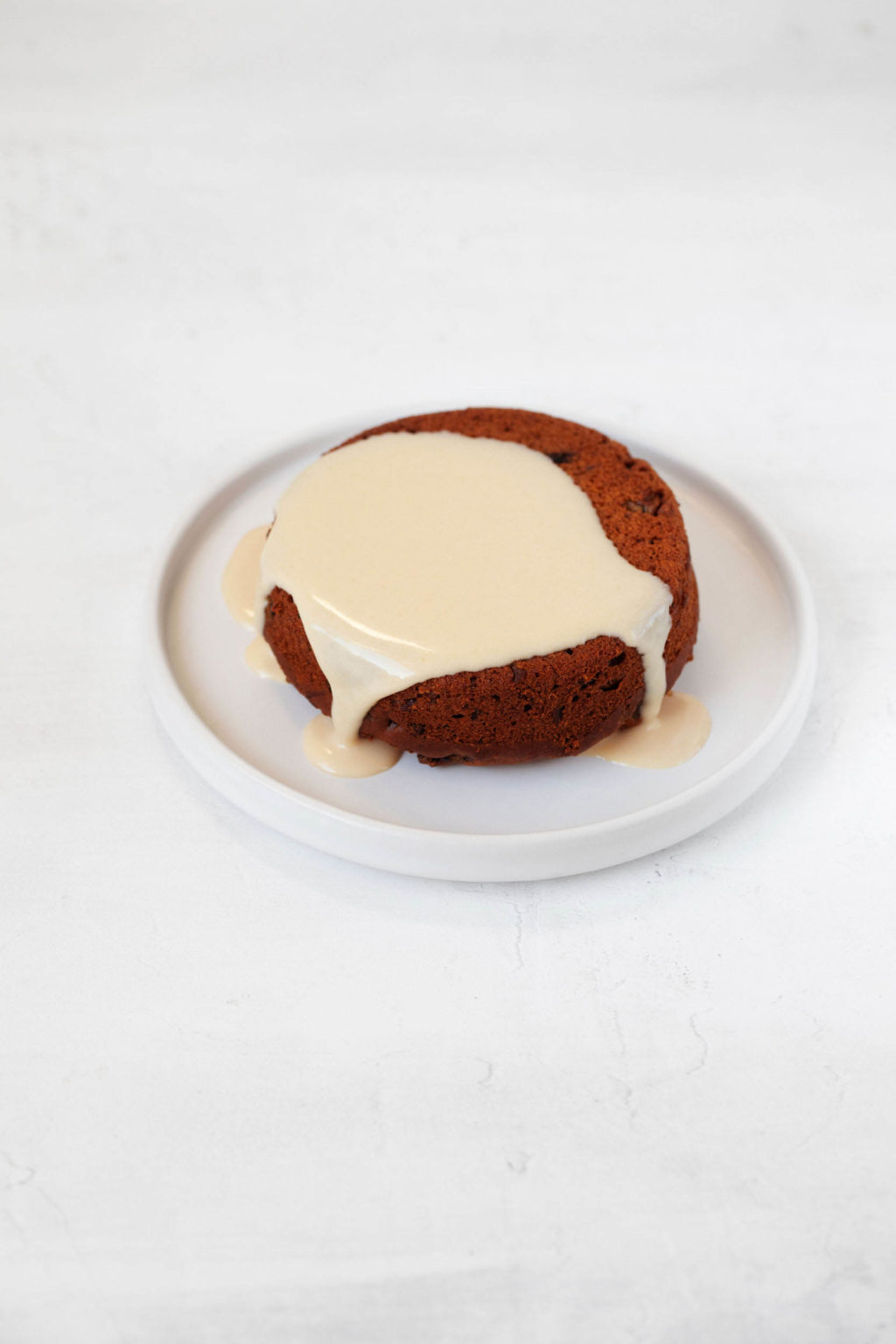A serving of vegan sticky toffee pudding has been topped with a creamy cashew sauce. It rests on a small white plate.
