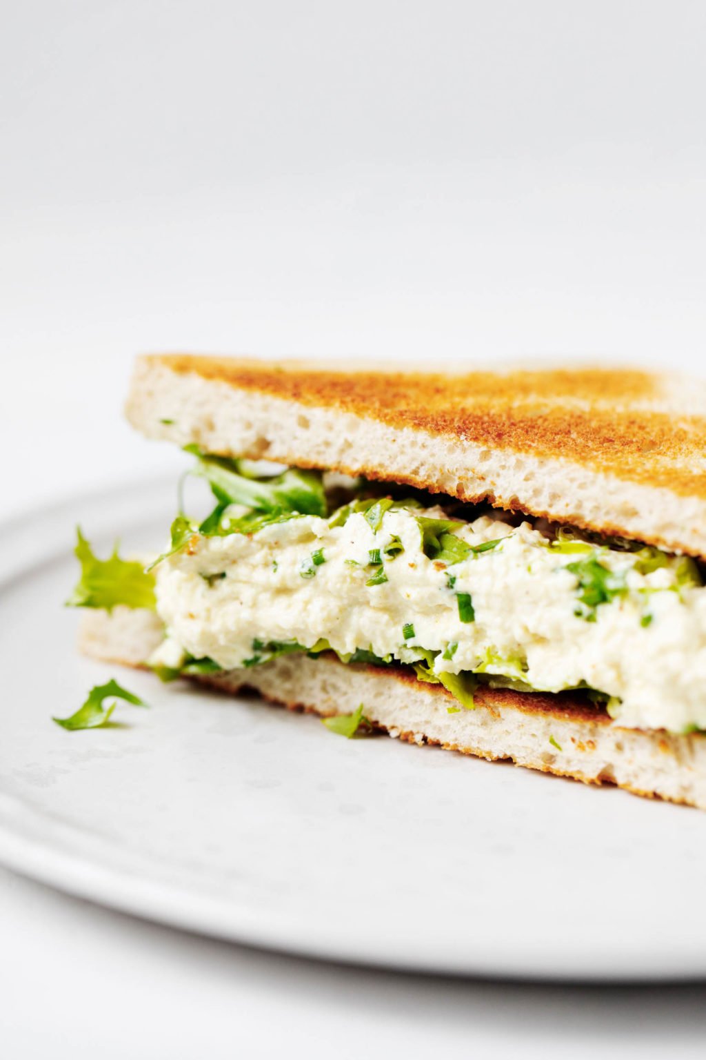 A toasted sandwich has been prepared with a vegan tofu egg salad. It's plated on a white ceramic plate.