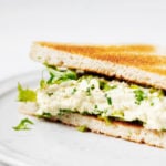 A toasted sandwich has been prepared with a vegan tofu egg salad. It's plated on a white ceramic plate.