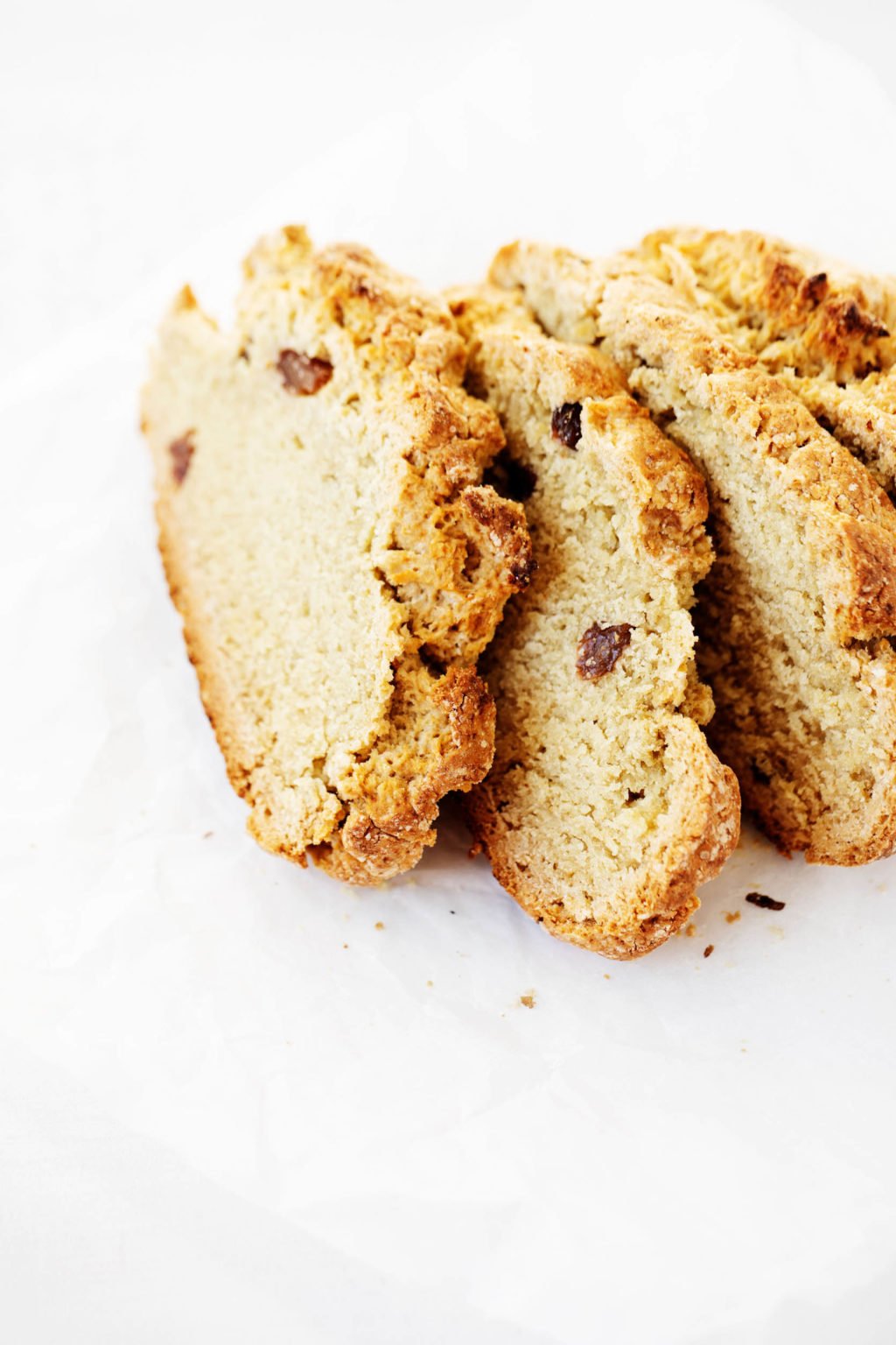 A few slices of vegan Irish soda bread, lined up on a white sheet of parchment paper.