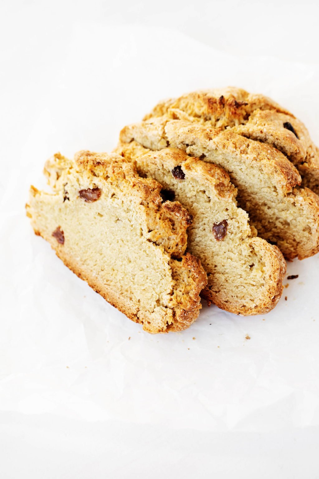 Four rustic slices of a dense, vegan Irish soda bread are placed on a white surface.