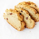 Four rustic slices of a dense, vegan Irish soda bread are placed on a white surface.