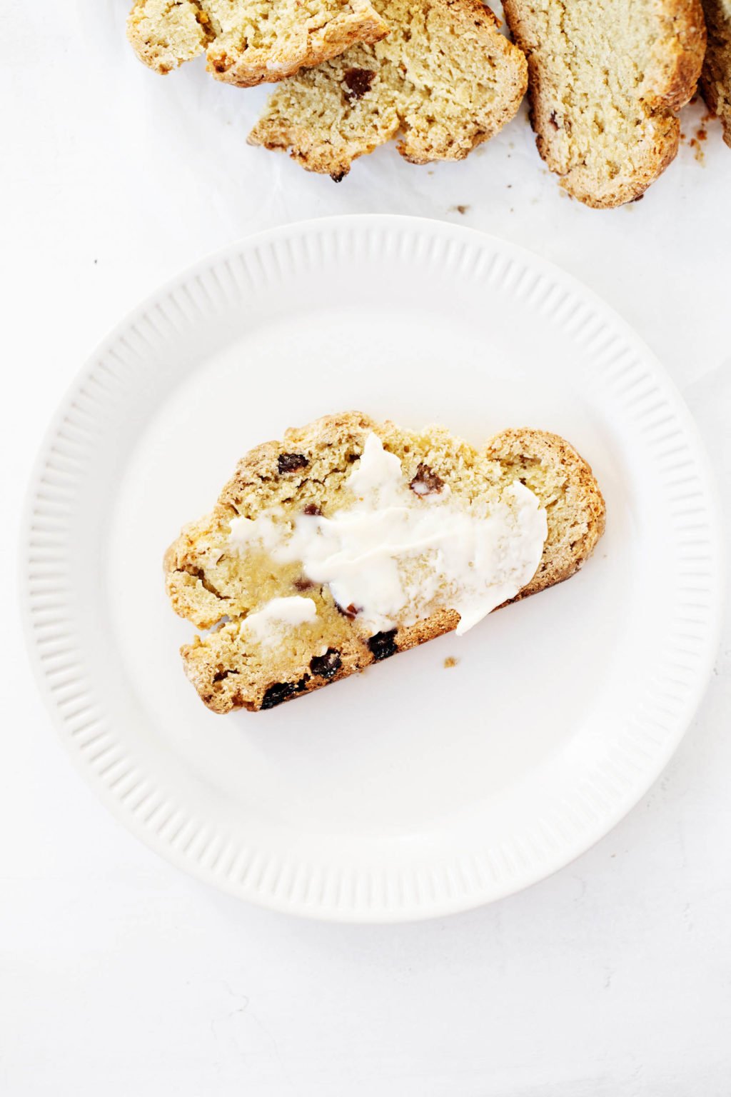 A small slice of vegan Irish soda bread has been topped with butter and served on a fluted white plate.