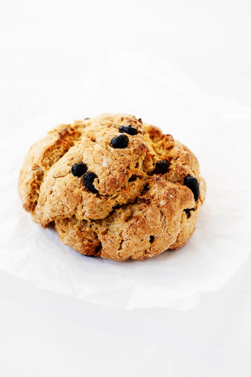 A round, rustic quick bread has been studded with currants and laid out on a sheet of white parchment paper.