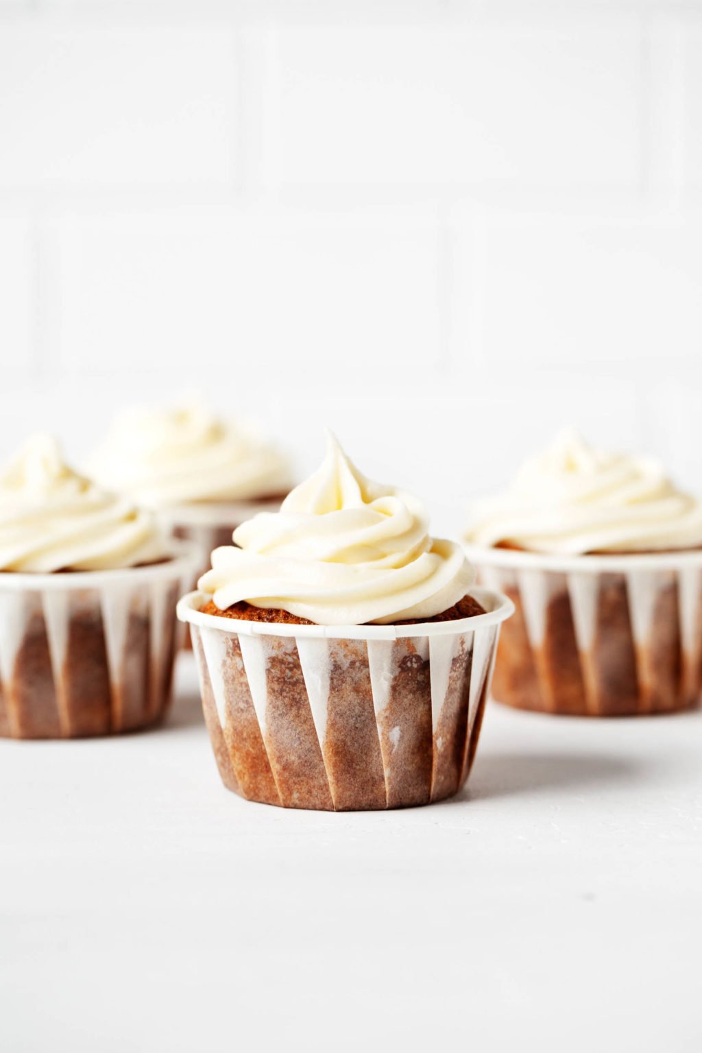 Frosted vegan carrot cake cupcakes are lined up next to each other against a bright backdrop.