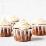 Frosted vegan carrot cake cupcakes are lined up next to each other against a bright backdrop.