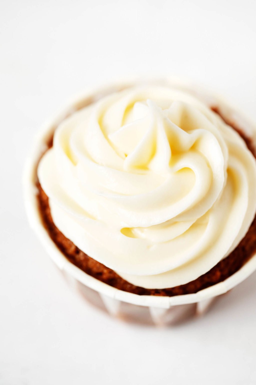 A vegan cupcake has been swirled with a rich, pale colored cream cheese frosting.