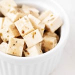 Un ramekin blanco y redondo se ha llenado con pequeños cubos de queso feta de tofu vegano con hierbas.