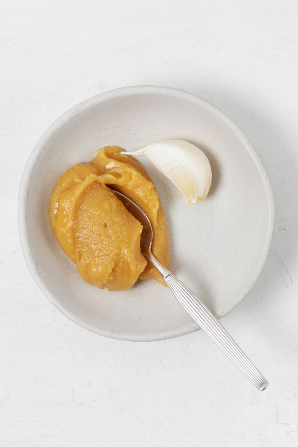 White miso and a clove of garlic and lying in a small, white pinch bowl.