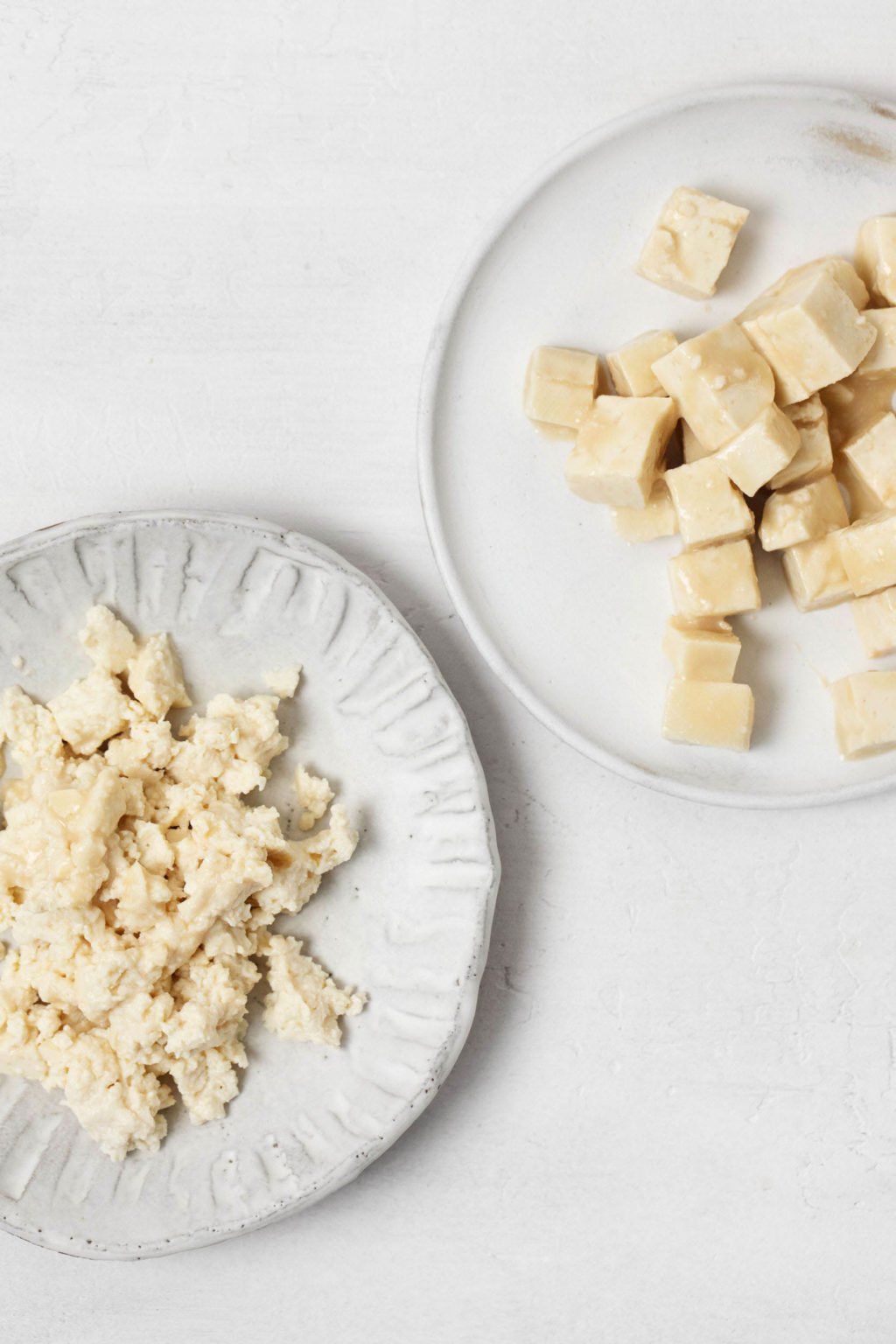 Tofu has been crumbled and cubed. The prepared protein is served on two small plates.