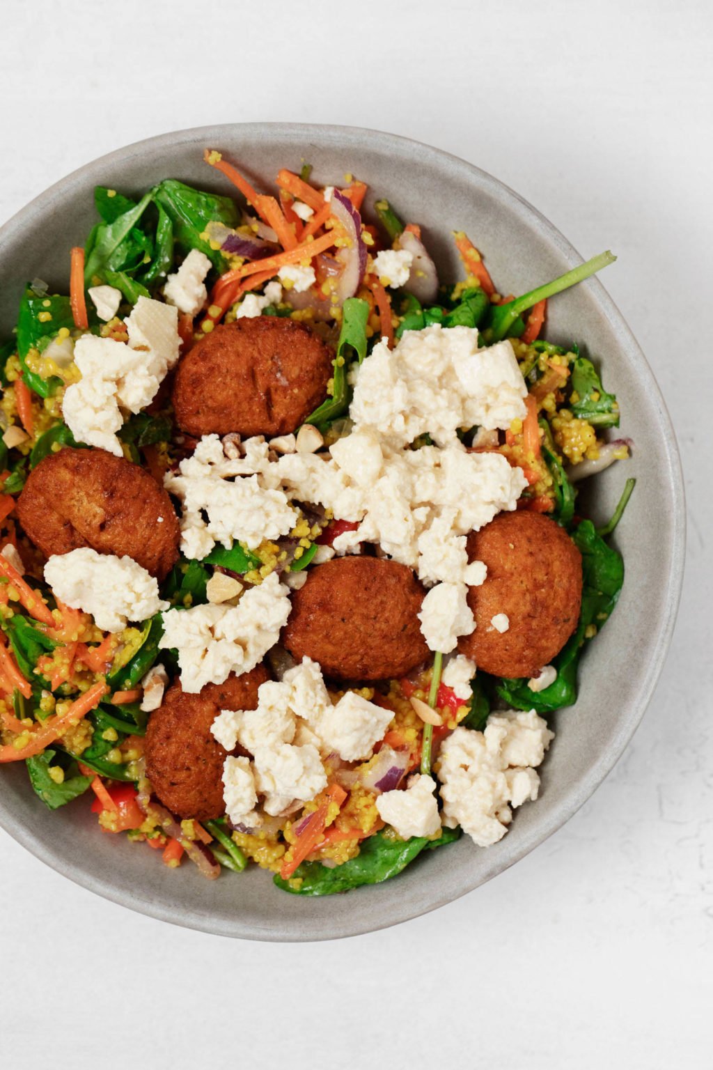Falafel, greens, and vegan feta cheese are piled into a round serving bowl.