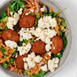 Falafel, greens, and vegan feta cheese are piled into a round serving bowl.