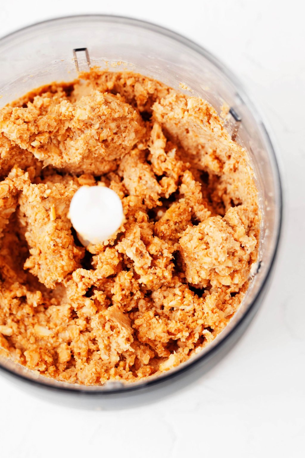The bowl of a food processor has been filled with crumbled tempeh, herbs, and ground walnuts.