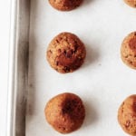 A silver rimmed baking sheet is covered with a sheet of parchment and freshly baked tempeh meatballs.