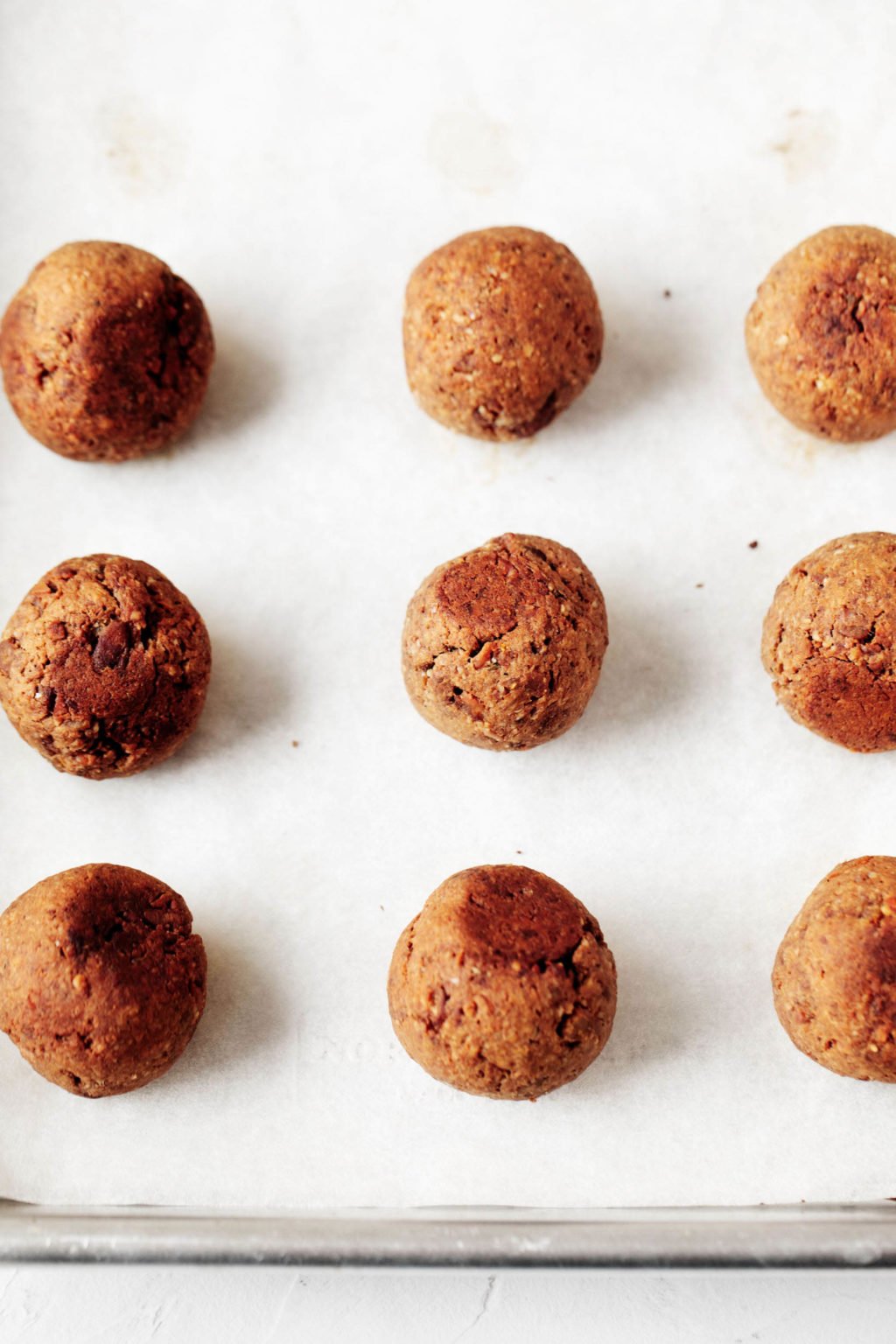 A parchment lined, silver baking sheet holds a tray of baked, crispy, plant-based meatballs.