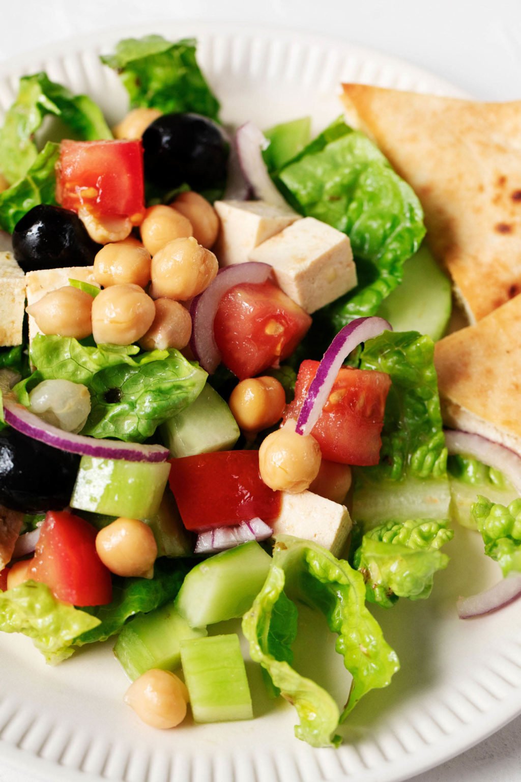 A zoomed in, overhead image of a fresh, summery salad with romaine, tofu, chickpeas, and tomatoes.