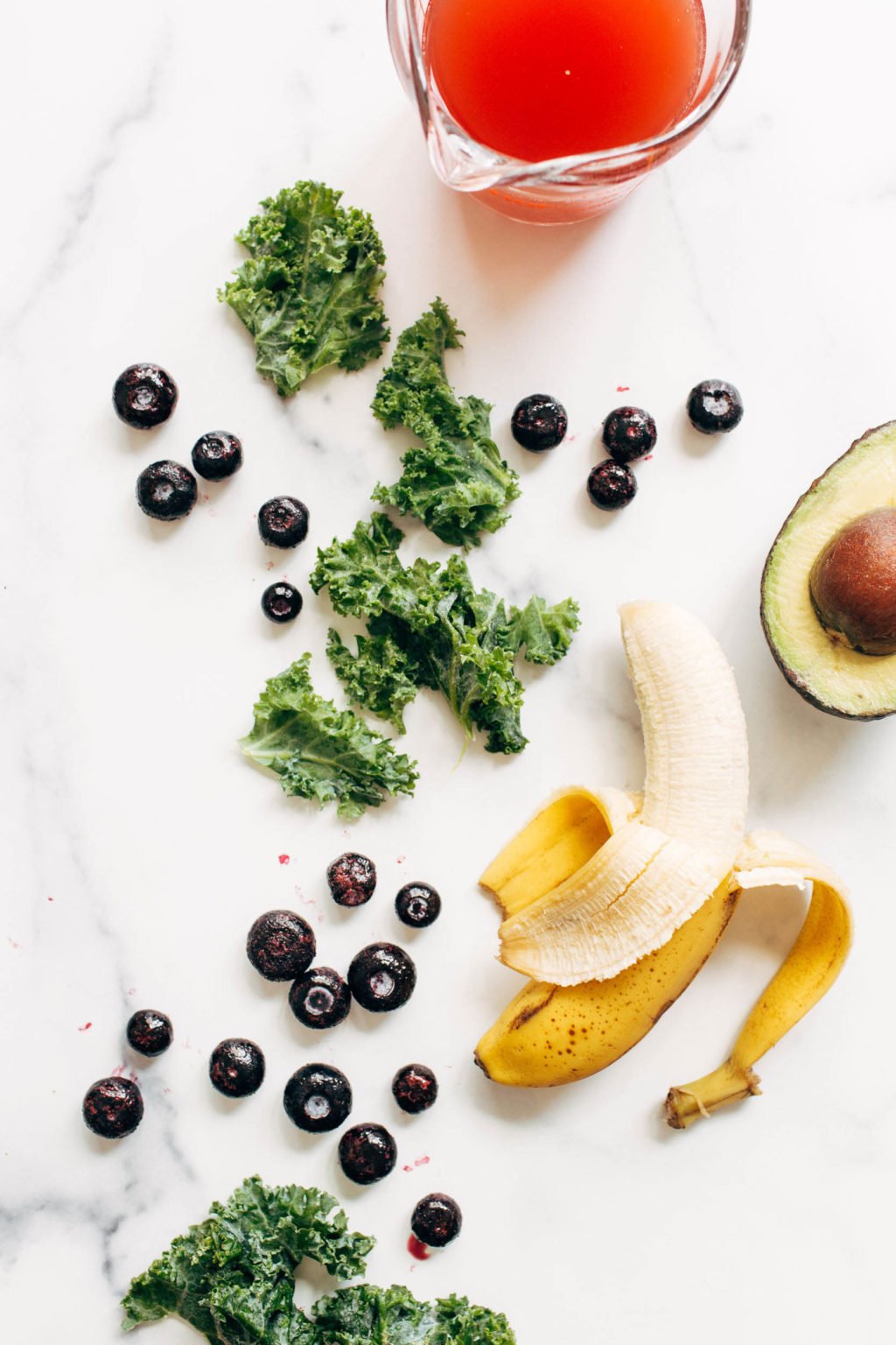 Fruits, vegetables, and greens are laid out on a white marble surface.