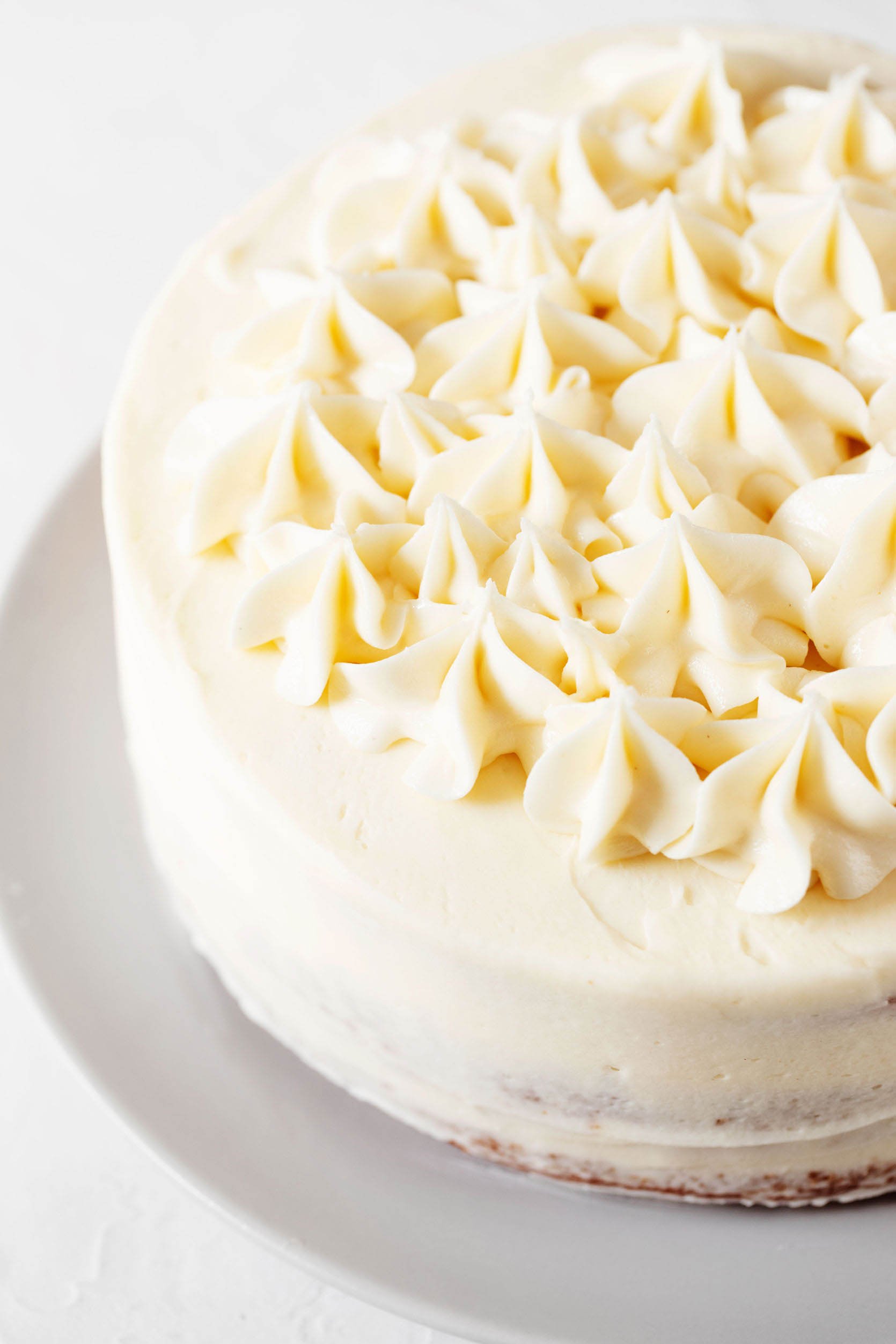 An angled photograph of a white, decorated cake that is resting on a round plate. It's covered in piped buttercream stars.